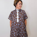 Woman wearing a brown floral dress with a white collar against a plain background