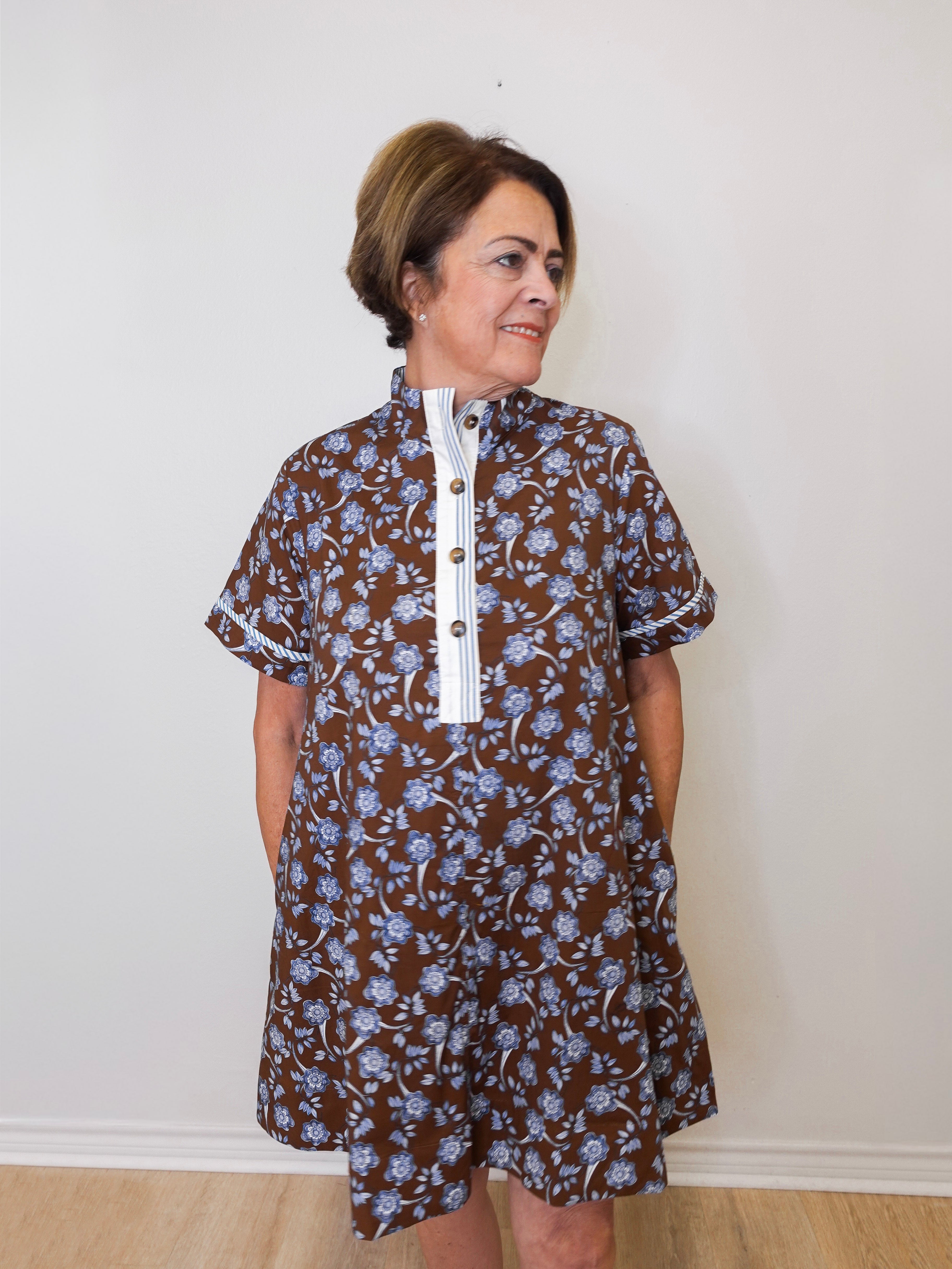 Woman wearing a brown floral dress with a white collar against a plain background