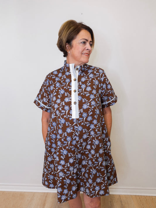 Woman wearing a brown floral dress with a white collar against a plain background