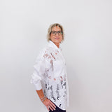 Person wearing a white floral blouse against a plain background