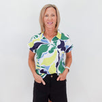 Woman wearing a colorful patterned shirt and black shorts against a white background