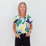 Woman wearing a colorful patterned shirt and black shorts against a white background