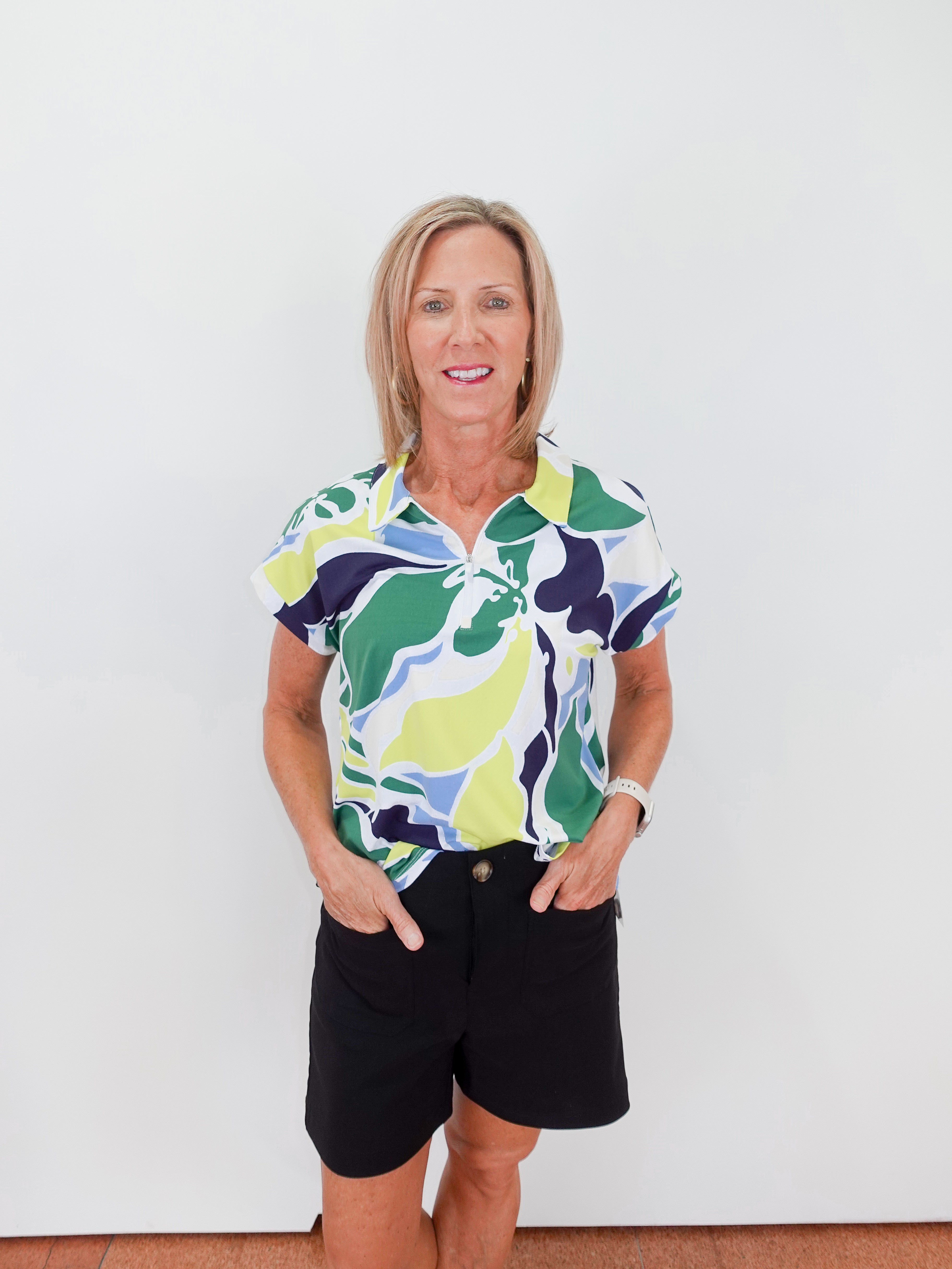 Woman wearing a colorful patterned shirt and black shorts against a white background