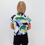 Person wearing a colorful patterned shirt and black shorts against a white wall.