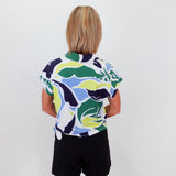 Person wearing a colorful patterned shirt and black shorts against a white wall.