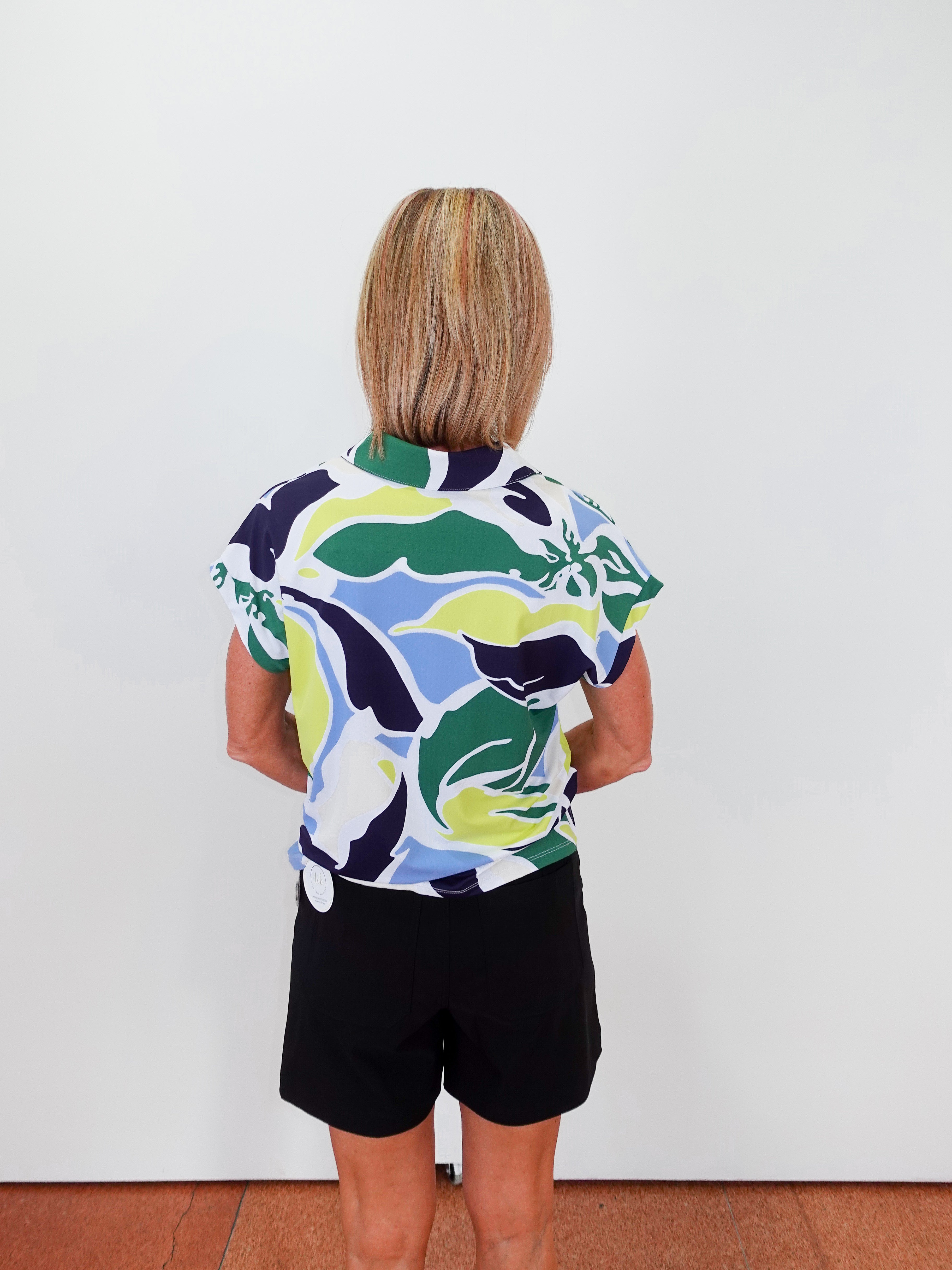Person wearing a colorful patterned shirt and black shorts against a white wall.