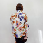 Person wearing a colorful floral shirt against a white wall