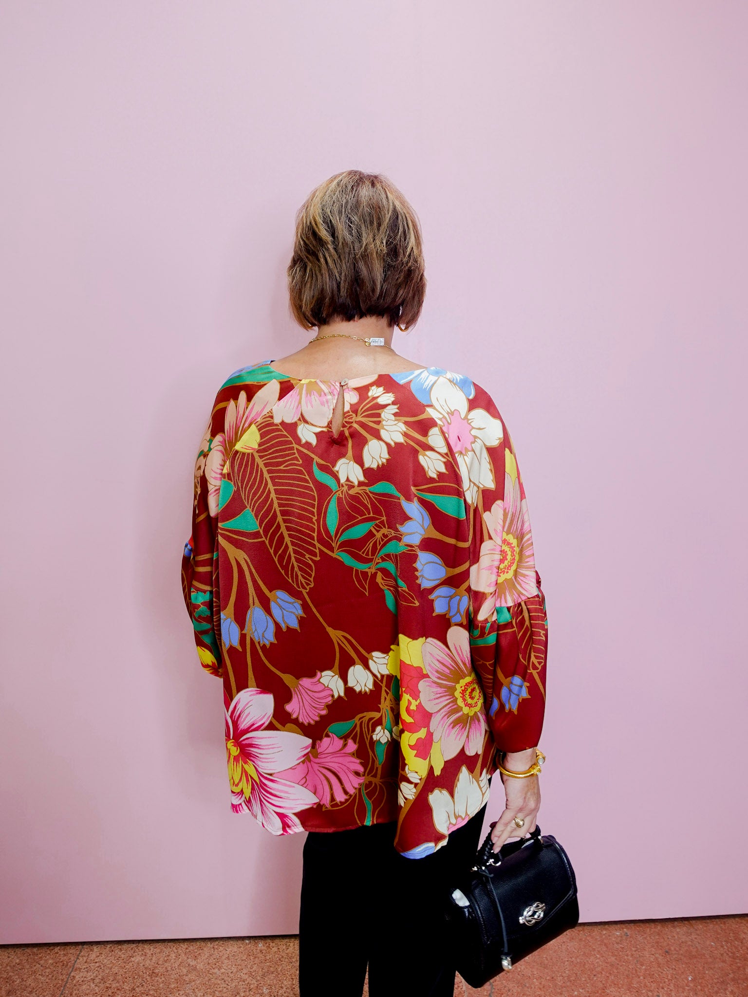 Person wearing a colorful floral jacket against a pink wall