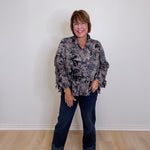 Woman wearing a patterned blouse and jeans standing against a plain white wall.