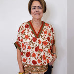 women wearing a beige floral print short sleeve top with black pants against a white wall. 