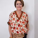 women wearing a beige floral print short sleeve top with black pants against a white wall. 