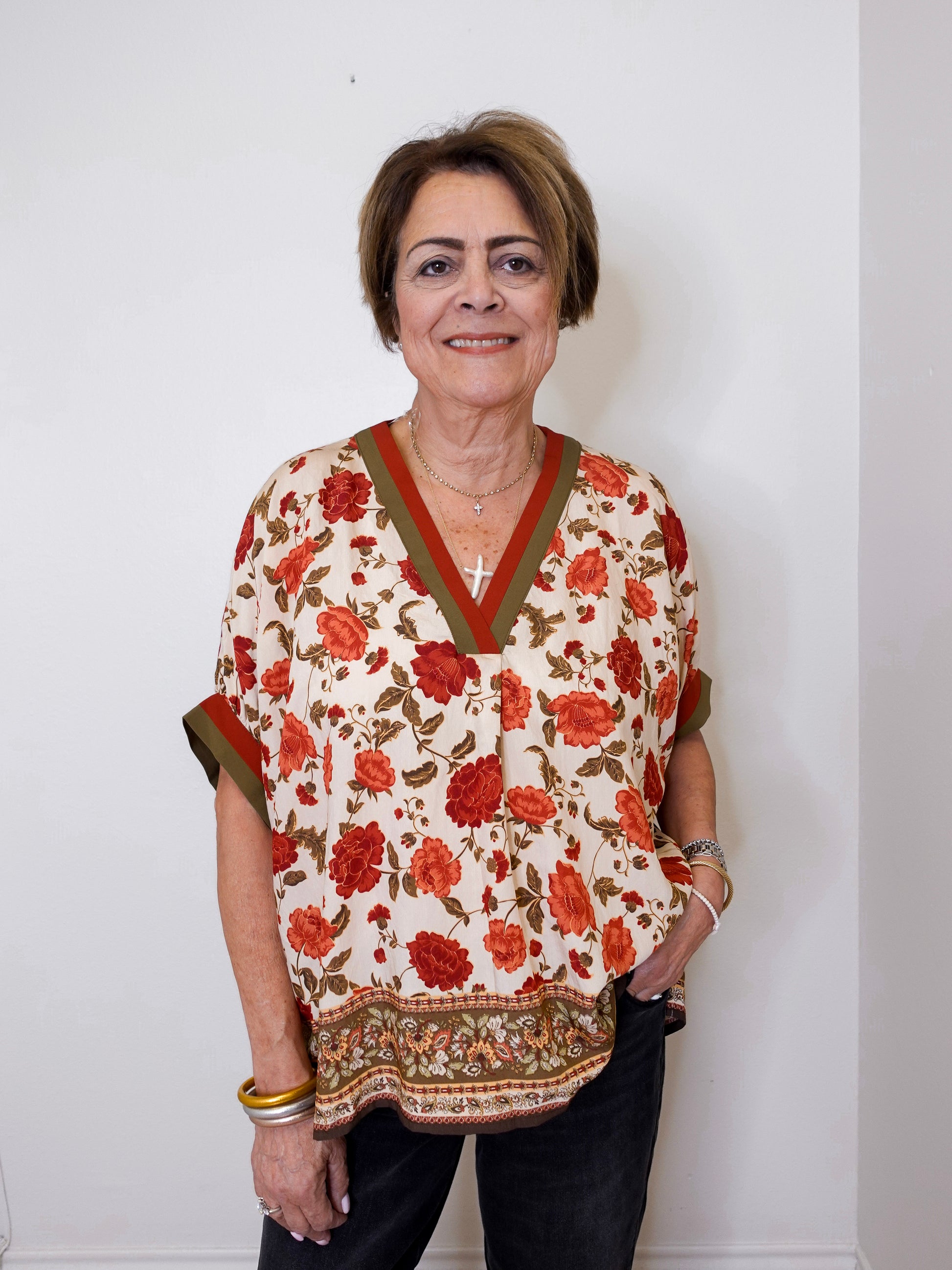 women wearing a beige floral print short sleeve top with black pants against a white wall. 