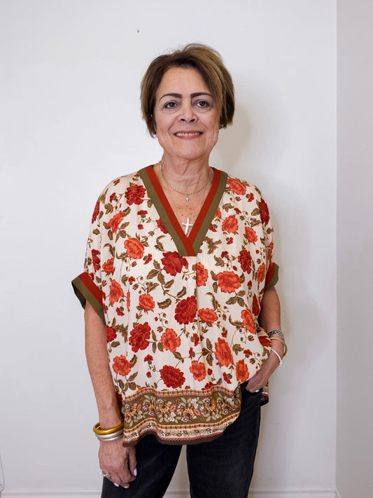 women wearing a beige floral print short sleeve top with black pants against a white wall. 