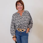 Woman wearing a patterned blouse and blue jeans against a plain background