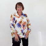 Woman wearing a colorful floral blouse and black shorts against a white background
