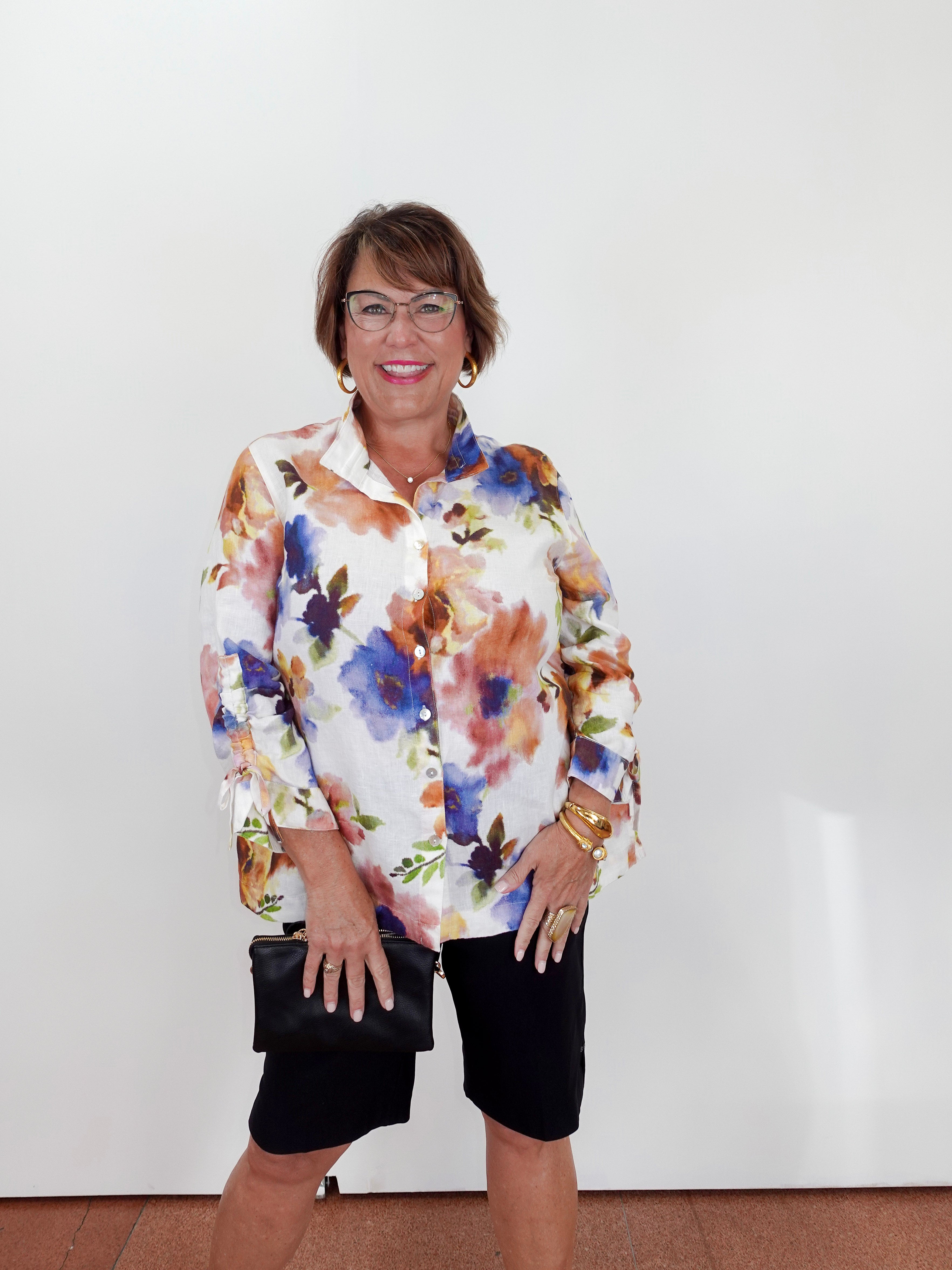 Woman wearing a colorful floral blouse and black shorts against a white background