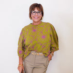 Woman wearing a green floral blouse and beige pants against a white background