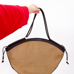 Person holding a straw handbag with black accents on a white background