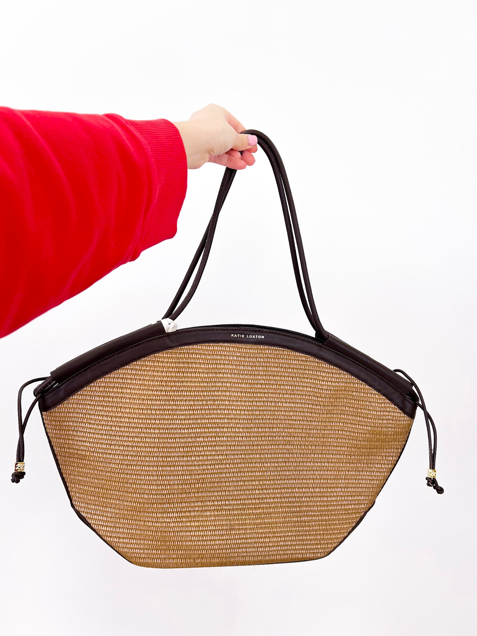 Person holding a straw handbag with black accents on a white background