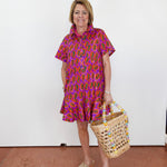 Woman wearing a colorful dress holding a woven basket against a white wall.