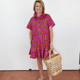 Woman wearing a colorful dress holding a woven basket against a white wall.