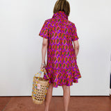 Person wearing a colorful patterned dress holding a woven bag on a red floor.