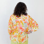 Person wearing a colorful floral blouse and green pants on a white background