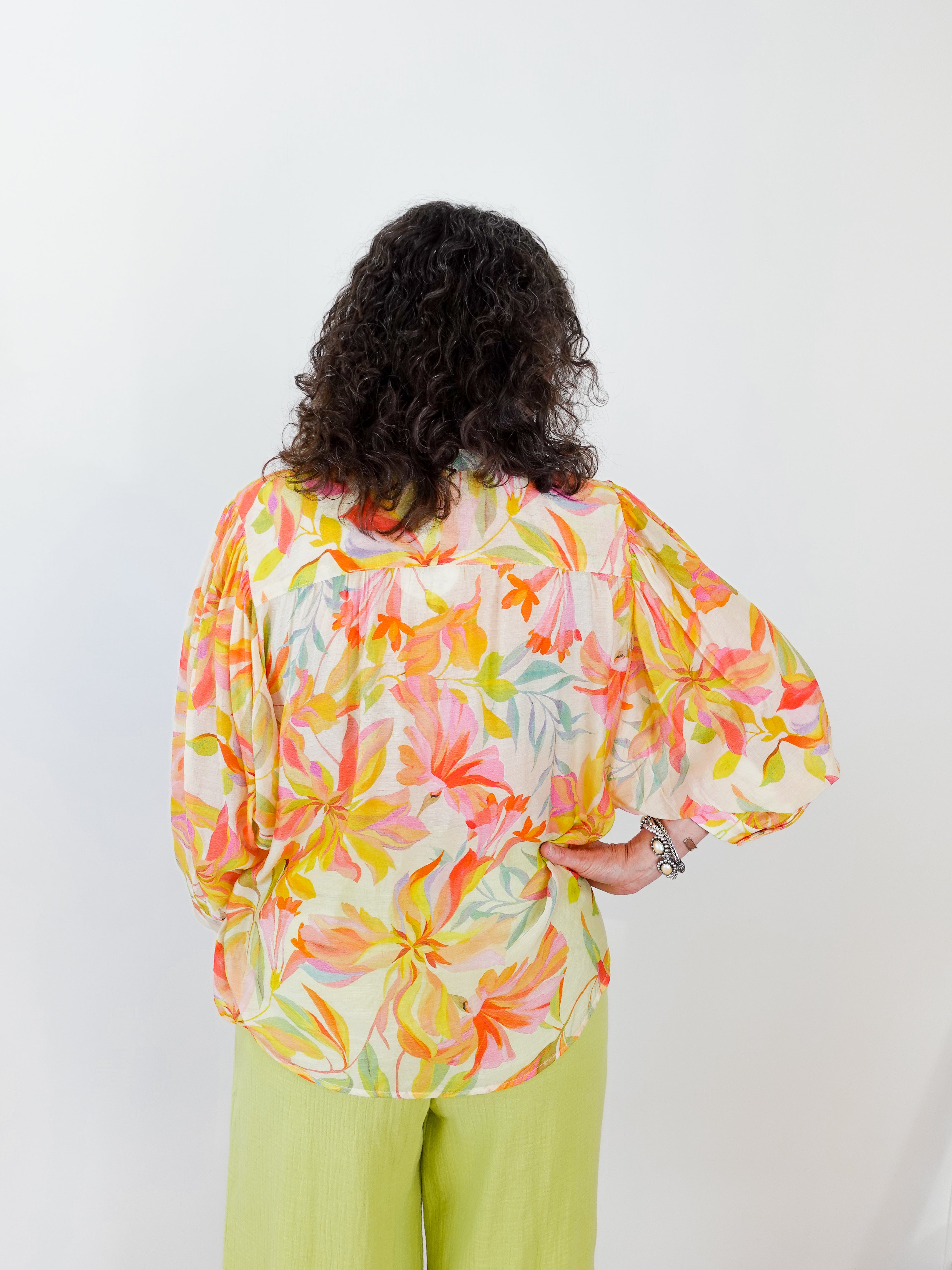 Person wearing a colorful floral blouse and green pants on a white background