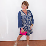 Woman wearing a blue floral dress with a pink clutch against a white background