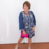 Woman wearing a blue floral dress with a pink clutch against a white background