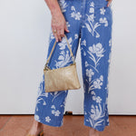 Person wearing blue floral pants holding a beige handbag indoors.