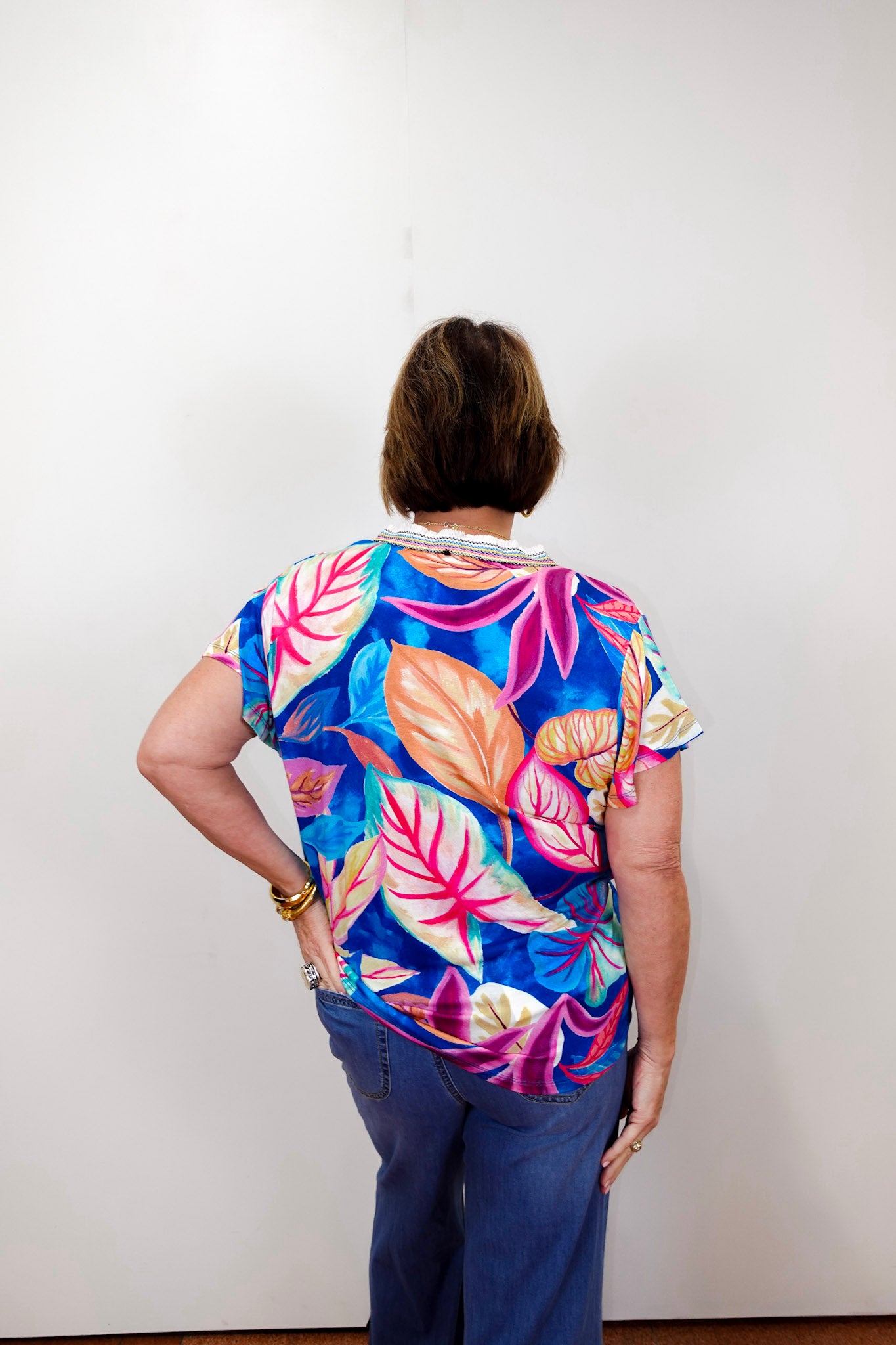 Person wearing a colorful floral shirt with their back to the camera on a white background
