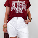 Person wearing a maroon t-shirt with a logo and white shorts against a plain background