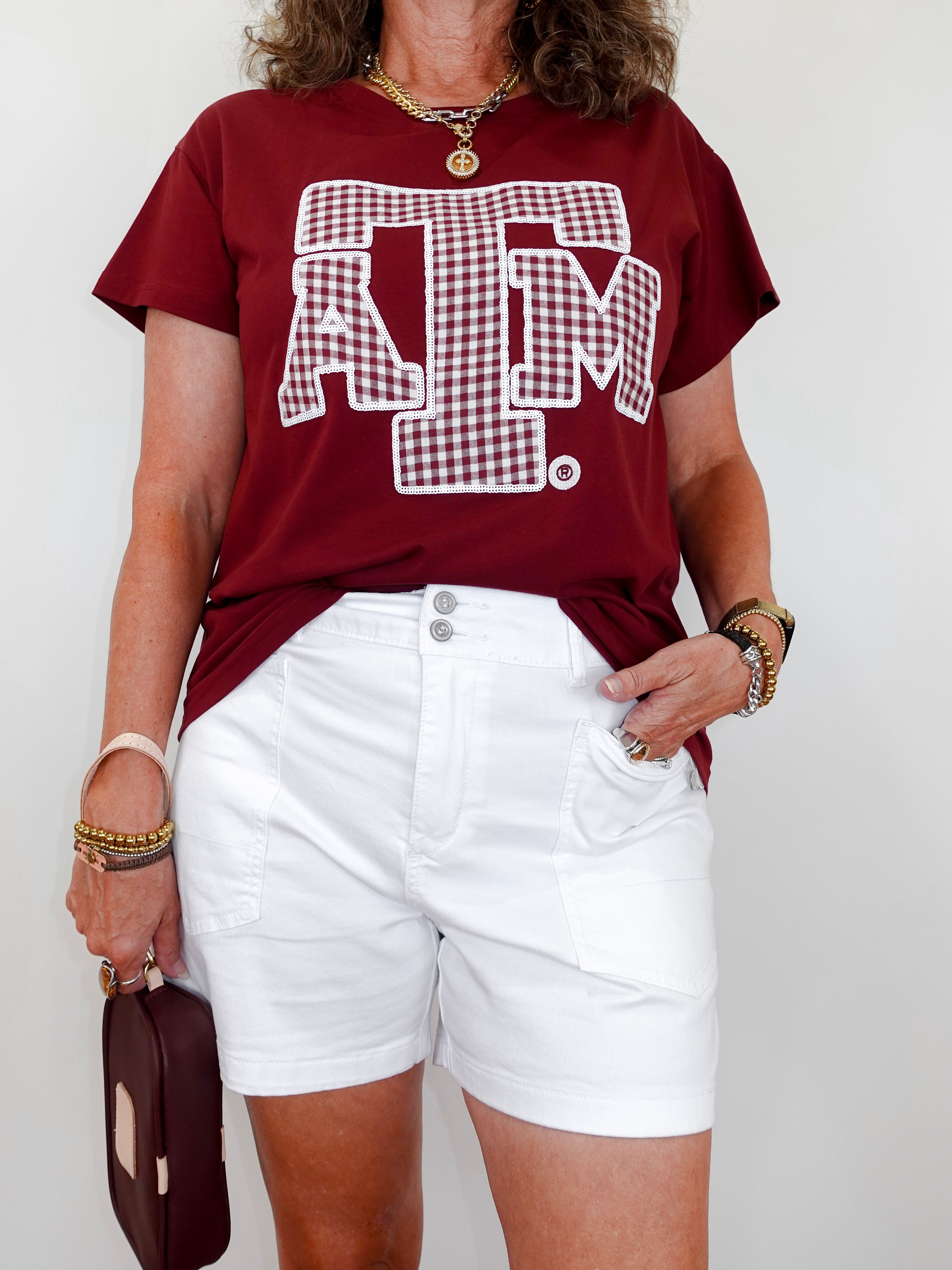 Person wearing a maroon t-shirt with a logo and white shorts against a plain background