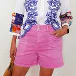 Person wearing a white shirt with blue floral embroidery and pink shorts, holding a brown bag.