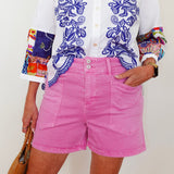 Person wearing a white shirt with blue floral embroidery and pink shorts, holding a brown bag.