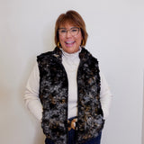 Woman wearing a patterned vest over a white turtleneck against a plain background