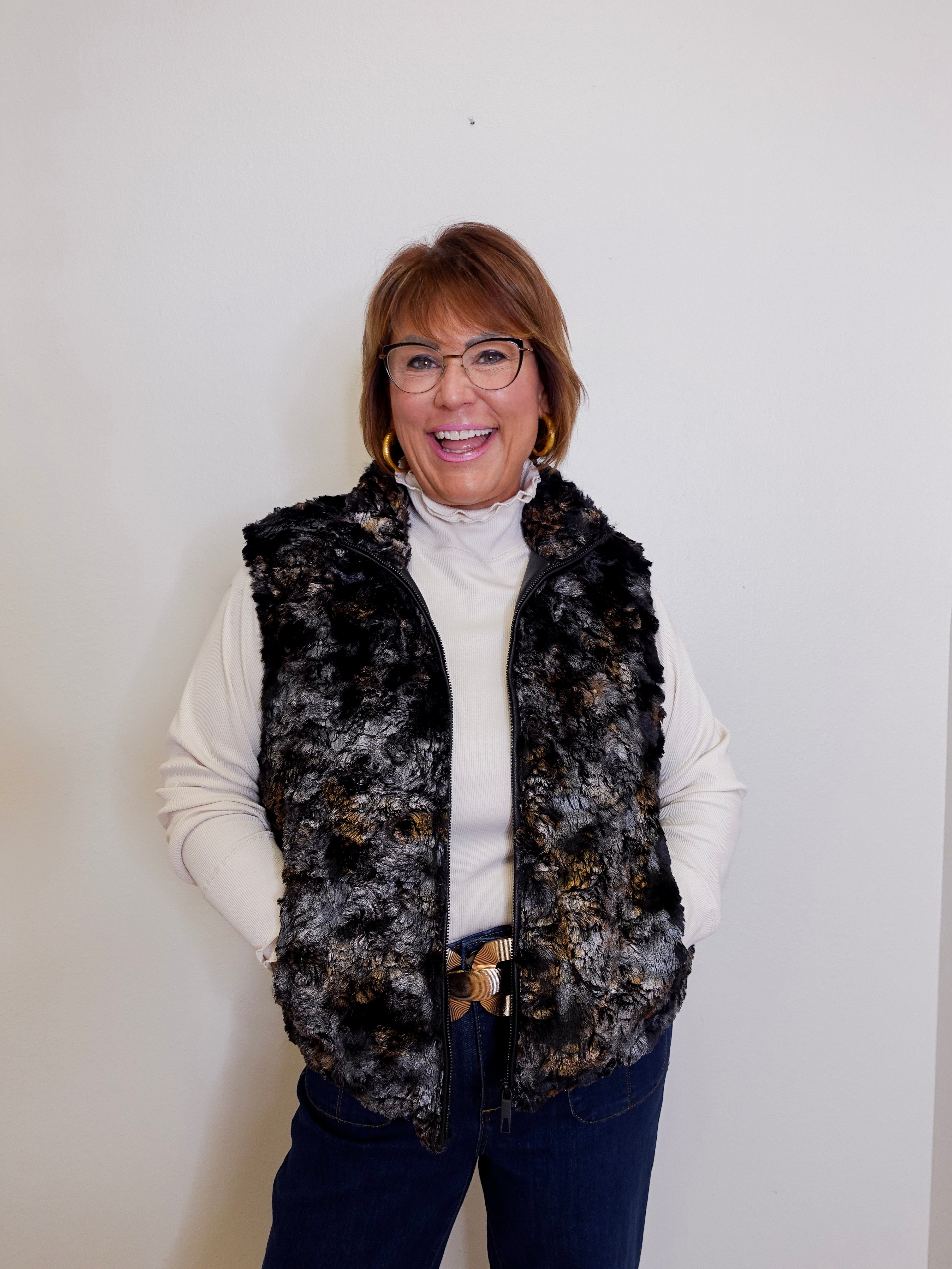 Woman wearing a patterned vest over a white turtleneck against a plain background