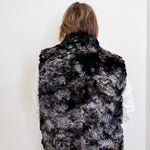 Person wearing a black and gray patterned fur vest against a white background
