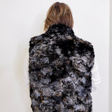 Person wearing a black and gray patterned fur vest against a white background