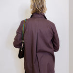 Person wearing a brown pinstripe coat against a white wall