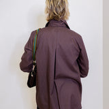 Person wearing a brown pinstripe coat against a white wall