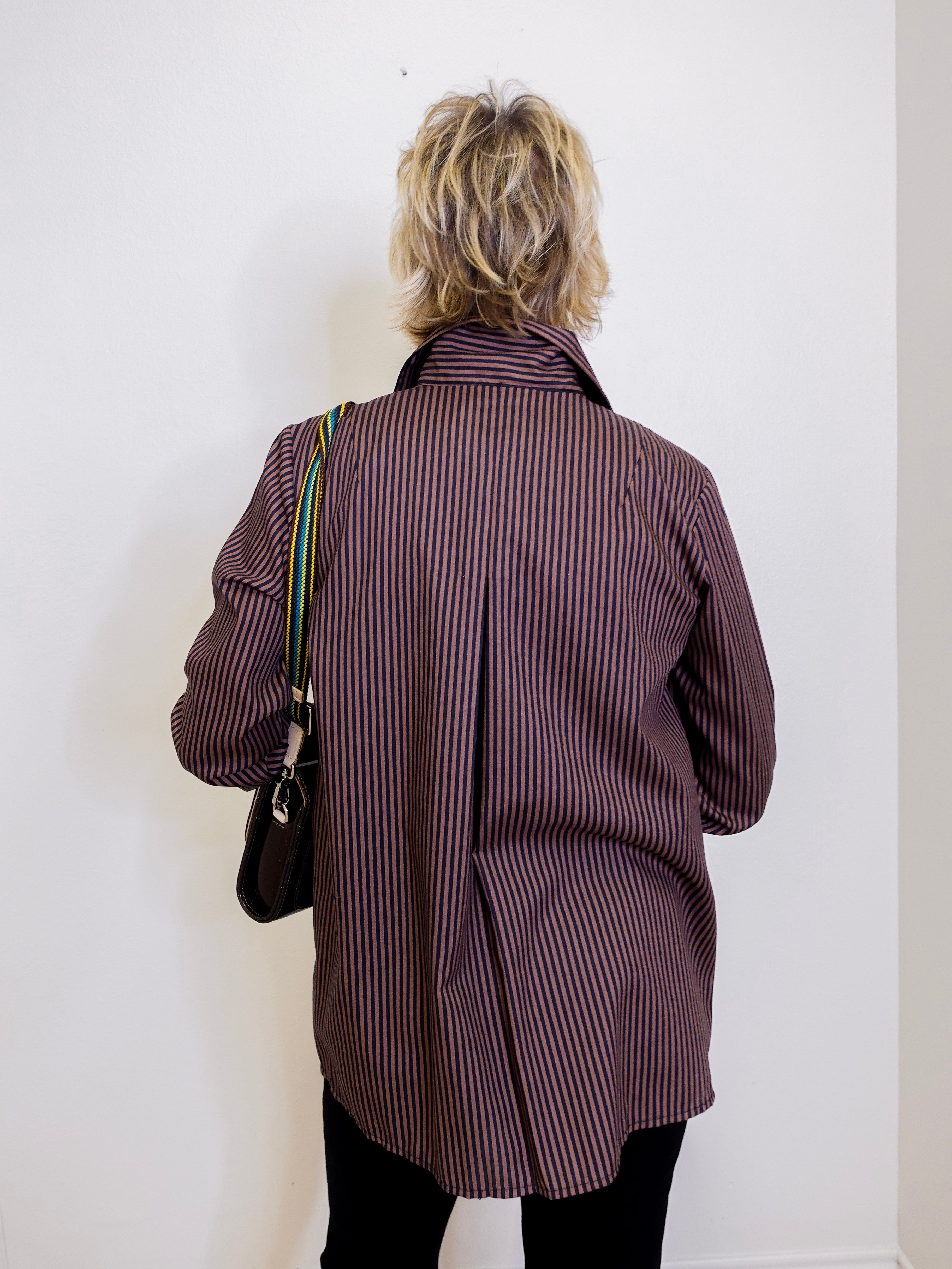 Person wearing a brown pinstripe coat against a white wall