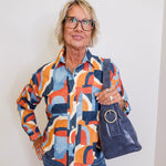 Person wearing a colorful patterned shirt and holding a blue handbag against a white background