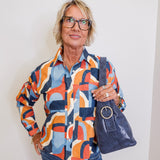 Person wearing a colorful patterned shirt and holding a blue handbag against a white background