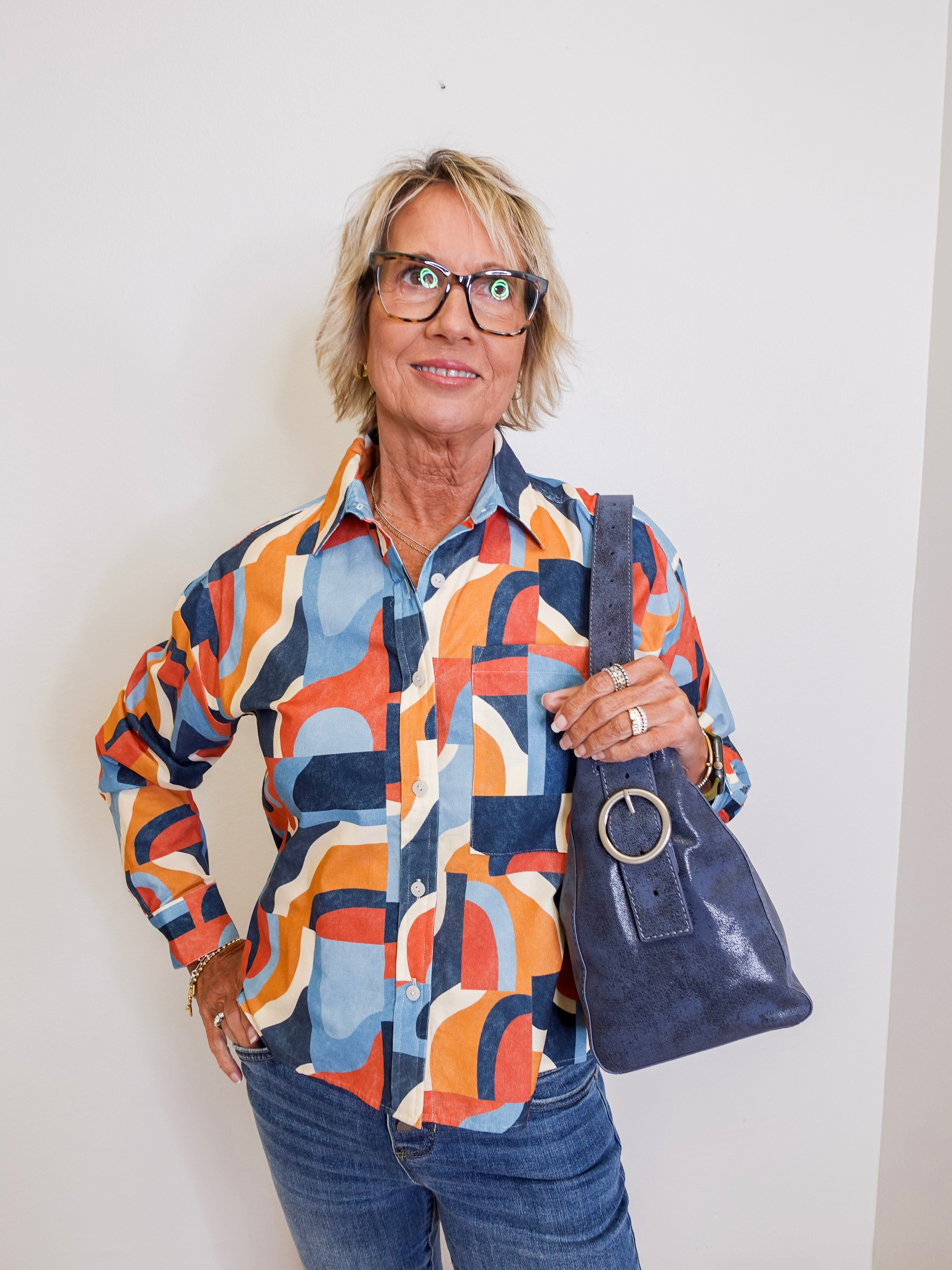 Person wearing a colorful patterned shirt and holding a blue handbag against a white background