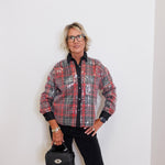 Person wearing a plaid jacket and holding a black handbag against a white background