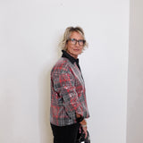 Person wearing a red and black plaid jacket against a white wall