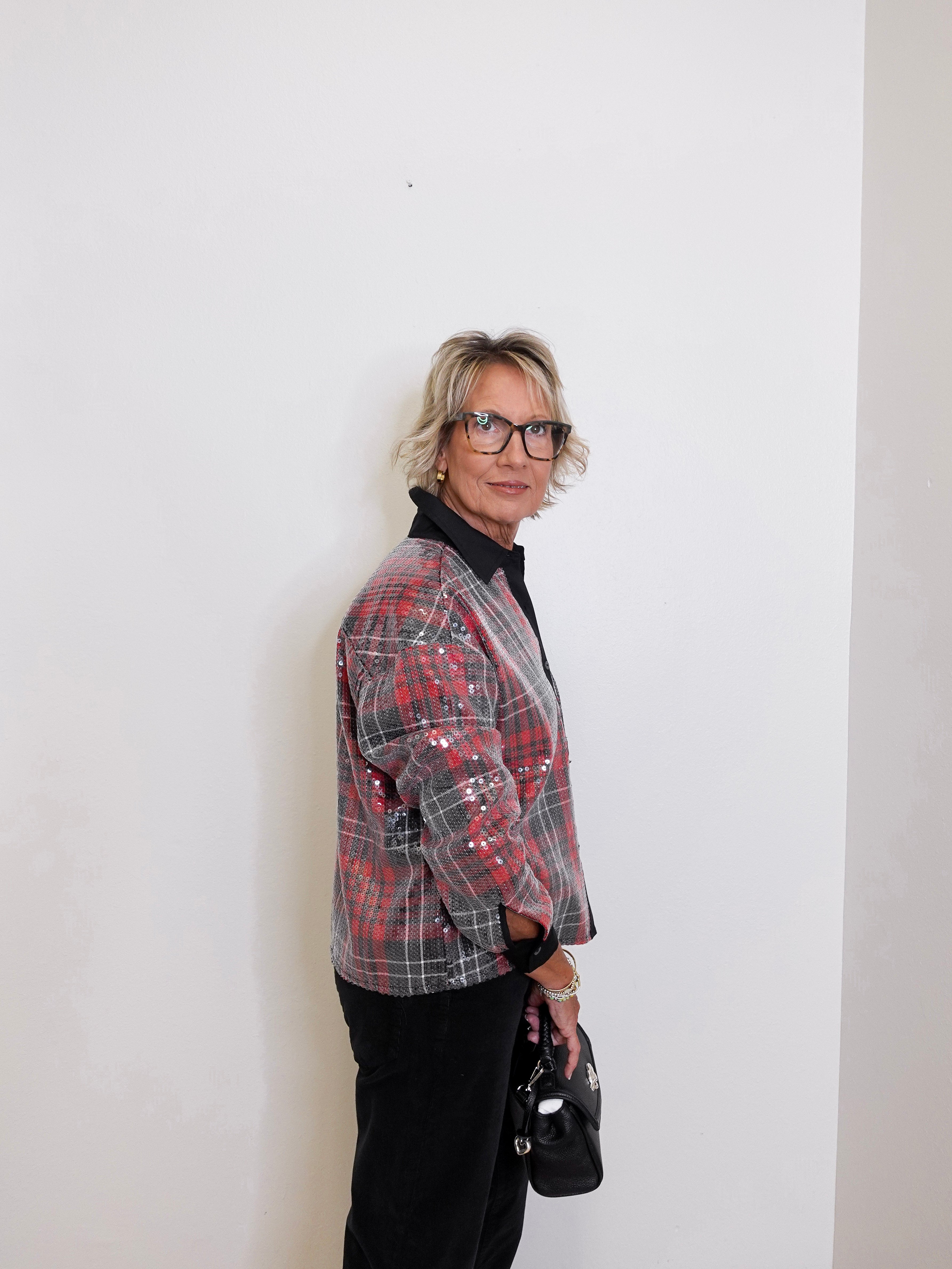 Person wearing a red and black plaid jacket against a white wall