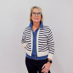 Woman wearing a striped cardigan over a denim shirt with a plain background